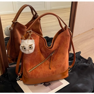 Detail view of corduroy tote bag with leather base and owl charm on a mirrored floor