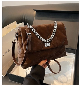 Détail d'un sac bandoulière matelassé marron avec fermoir argenté et chaîne épaisse