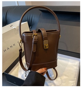 Détail du sac seau en cuir marron foncé avec boucles dorées et logo embossé