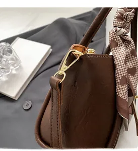 Detail of premium brown bucket bag featuring gold hardware and a patterned silk scarf