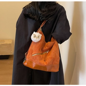 Detail of orange corduroy tote bag with leather base and owl plush charm on shoulder