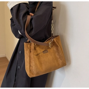 Detail of camel brown tote bag with quilted pattern and metal chain strap on model