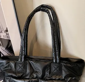 Detail shot of the black quilted texture and padded handles on this large puffer tote bag