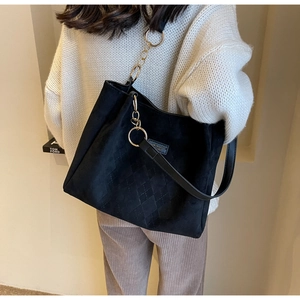 Detail of black suede tote bag featuring diamond quilted stitching and gold metal ring
