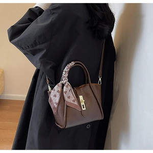 Detail of dark brown bucket bag with gold lock and decorative silk heart scarf
