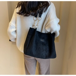 Detail of black quilted tote bag with gold chain strap and textured matte finish