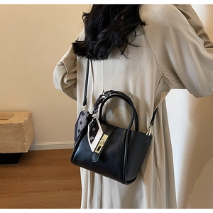 Close-up of black leather bucket bag with metallic twist lock and polka dot scarf
