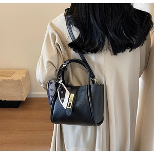 Detail of black leather bucket bag with gold lock and geometric silk scarf handle
