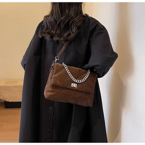 Sac bandoulière marron matelassé avec chaîne argentée porté sur un manteau de laine noir