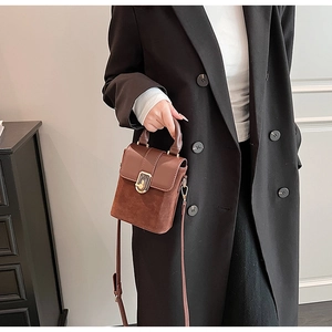 Detail of dark brown matte suede and leather handbag with gold clasp on black coat