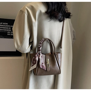 Detail of dark brown leather bucket bag with silk scarf on handle and gold metal buckle