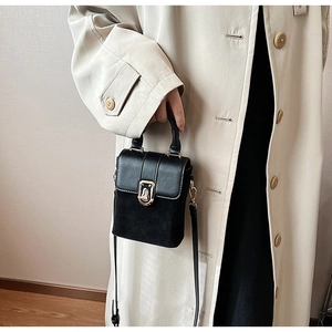 Detail shot of black crossbody bag with mixed texture and metal twist lock on a trench coat