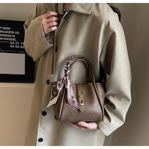 Detail of dark brown pleated leather bucket bag with gold lock and silk scarf handle