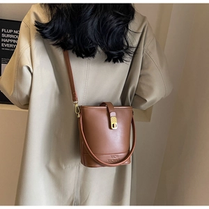 Détail d'un sac seau en cuir marron avec double bandoulière et boucle en métal doré