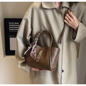 Detail of dark brown leather bucket bag with gold clasp and elegant printed silk scarf