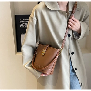Sac seau en cuir marron avec boucle dorée porté par un mannequin dans un décor épuré