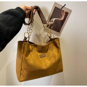 Detail of quilted mustard suede tote bag with elegant gold metal chain shoulder strap