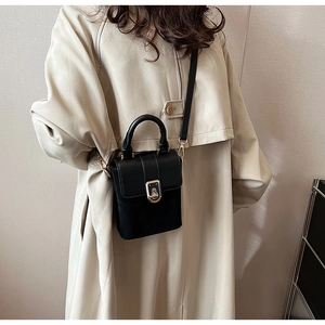 Detail of black crossbody bag with matte texture and gold hardware on beige coat