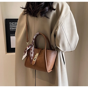 Brown bucket bag side view with decorative silk scarf and golden hardware on beige coat