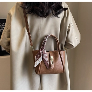 Brown bucket bag styled as a crossbody on a model in a trench coat with silk scarf detail