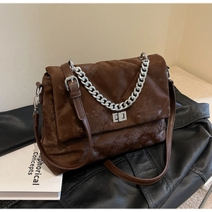 Détail du cuir matelassé marron vintage avec une grosse chaîne argentée sur le sac