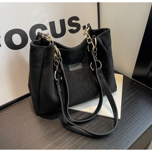 Detail of black quilted tote bag with gold chain strap and metal logo on matte leather