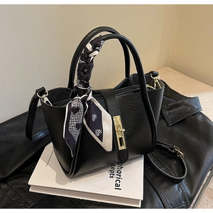 Close-up of black textured leather handbag with gold twist lock and silk scarf detail