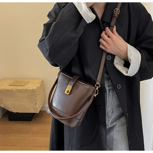 Détail d'un sac seau en cuir marron foncé avec ferrures dorées et logo NICH embossé