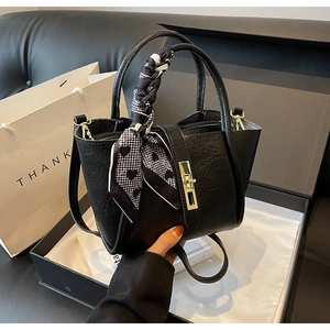 Close-up of black leather bucket bag with gold clasp and decorative heart scarf in a gift box