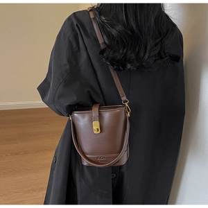 Détail du logo de marque embossé sur le sac seau en cuir marron foncé avec boucles dorées