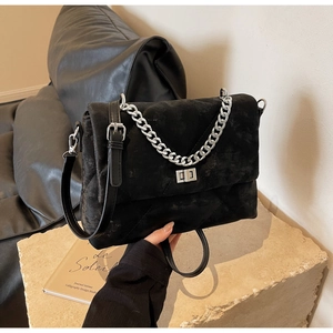 Détail d'un sac bandoulière en daim noir matelassé avec chaîne argentée et fermoir carré