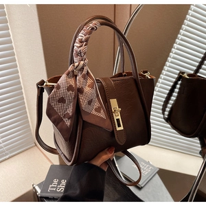 Detail of retro dark brown bucket bag with gold clasp and heart pattern scarf on handle