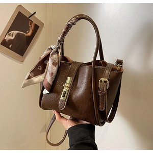 Close-up of vintage brown bucket bag with gold clasp and heart print silk scarf on handle