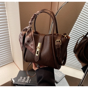 Detail of dark brown bucket bag featuring gold twist lock and heart pattern silk scarf handle