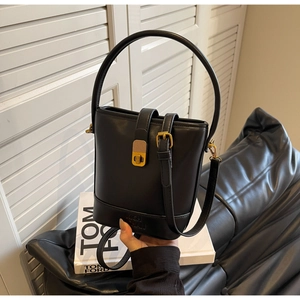 Détail du sac seau en cuir noir mat avec fermoir métallique doré rétro et poignée rigide