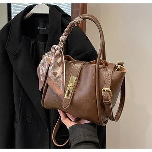 Detail view of brown textured leather bucket bag with silk scarf and gold twist lock