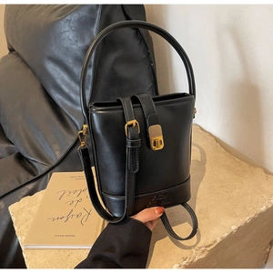 Détail du sac seau en cuir noir avec ferrures dorées et logo embossé sur socle en pierre