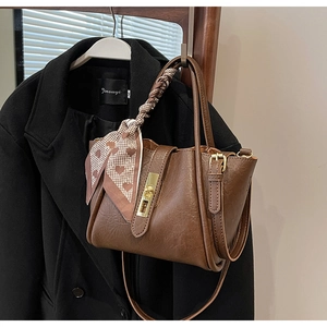 Detailed view of brown bucket bag with heart scarf and gold metal buckle latch