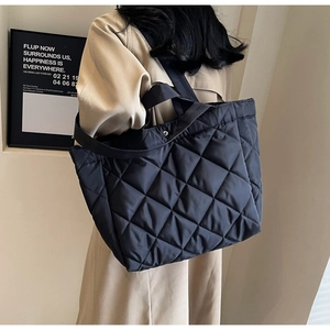 Detail of black quilted nylon tote bag with silver magnetic snap button and long strap