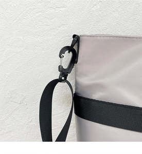 Detail of the black plastic carabiner hook and grey nylon strap on a crossbody tote bag