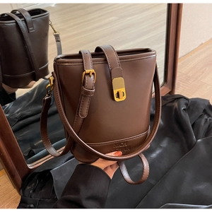 Détail du sac seau en cuir marron foncé avec boucles dorées et logo XICH XUAN embossé