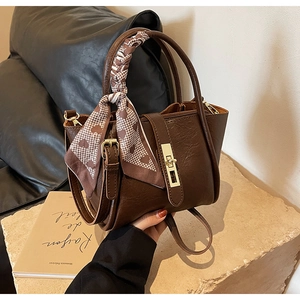 Detail of dark brown leather bucket bag with gold lock and houndstooth scarf handle