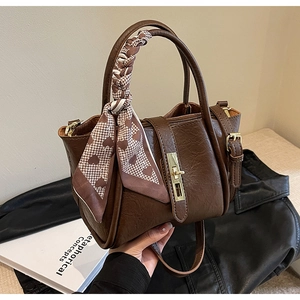 Close-up of retro brown leather bucket bag with silk scarf handle and gold lock hardware