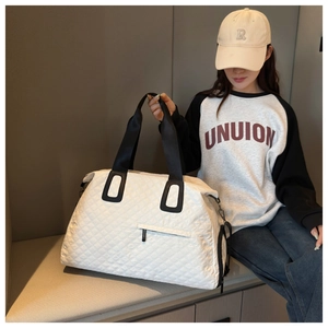 Bolso de viaje blanco acolchado con rombos y correas negras usado por una modelo casual