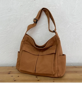 Dettaglio della borsa a tracolla in tela caramello con ampie tasche frontali con patta