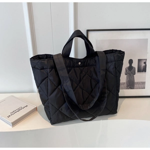 Close-up of black quilted nylon tote bag featuring metallic snap button and dual straps