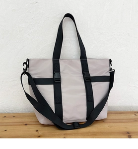 Detail of beige nylon tote bag featuring black utility webbing and adjustable strap