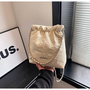 Close-up of cream quilted bucket bag with drawstring closure and metal chain strap