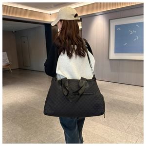 Bolso de viaje acolchado negro llevado por una modelo en un pasillo de hotel de lujo