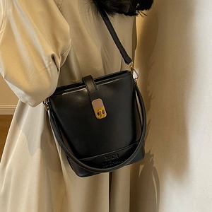Sac seau élégant en cuir noir avec ferrures dorées et bandoulière sur trench beige